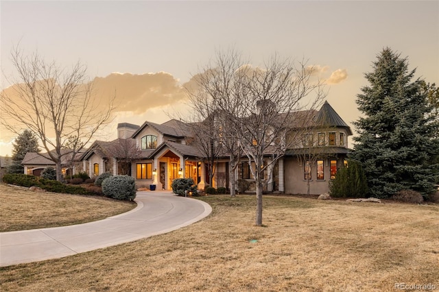view of front of property with stone siding, a chimney, a lawn, and curved driveway
