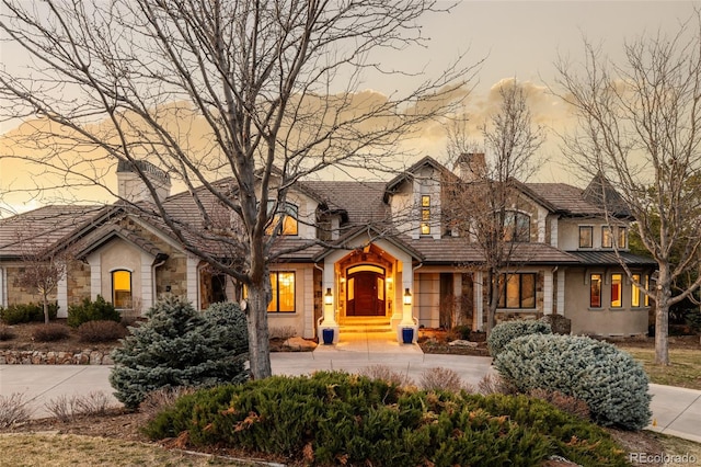 view of front of house with stone siding, concrete driveway, stucco siding, and a chimney