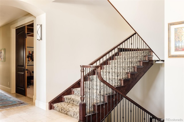 stairs with arched walkways, baseboards, and tile patterned flooring