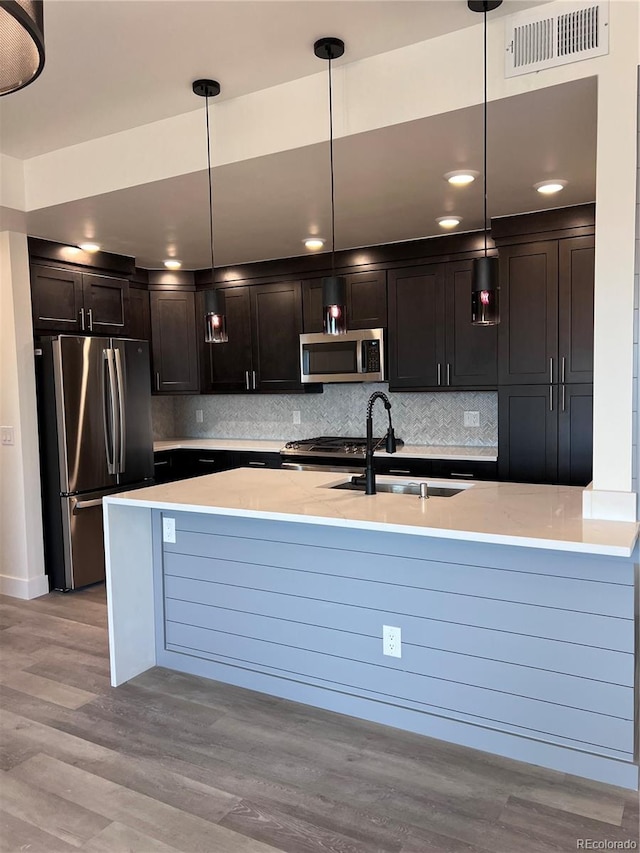 kitchen featuring light stone countertops, stainless steel appliances, sink, light hardwood / wood-style floors, and hanging light fixtures