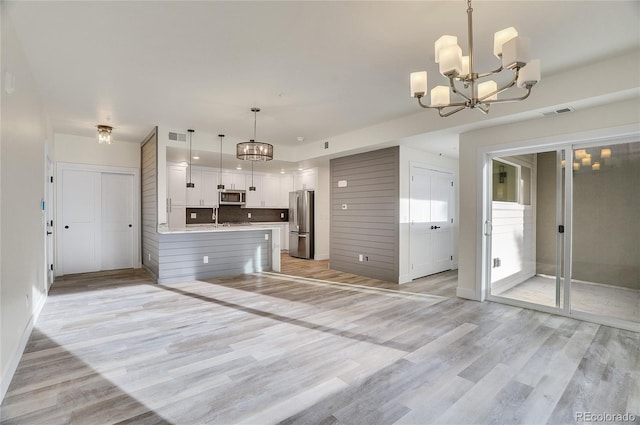 kitchen with decorative backsplash, stainless steel appliances, a notable chandelier, white cabinetry, and hanging light fixtures