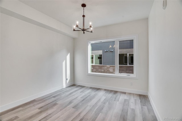 unfurnished room featuring a notable chandelier and light wood-type flooring