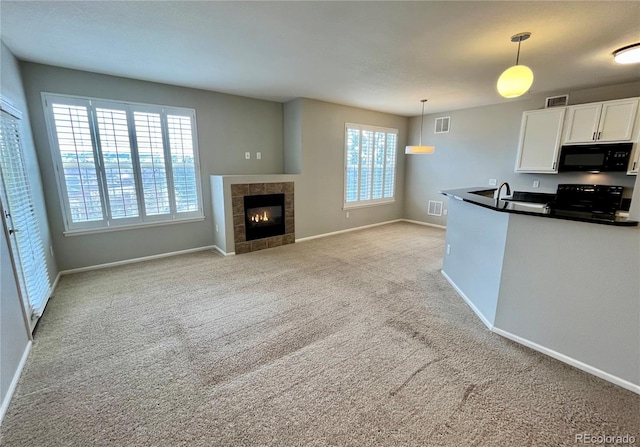 kitchen with white cabinetry, hanging light fixtures, light colored carpet, a tiled fireplace, and black appliances