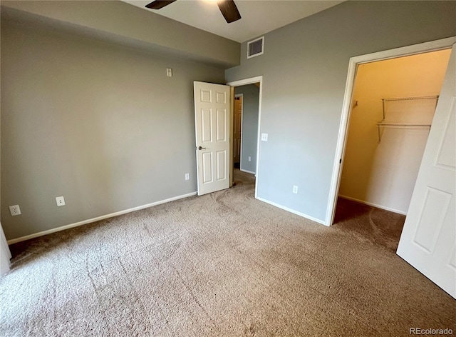 unfurnished bedroom with a closet, a spacious closet, ceiling fan, and carpet flooring