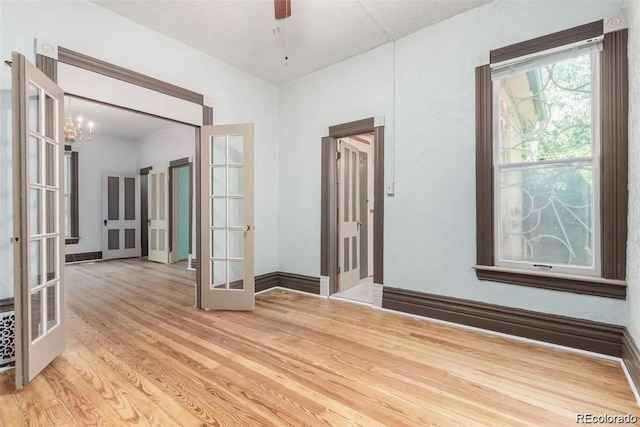 unfurnished room featuring ceiling fan with notable chandelier, french doors, and light wood-style flooring