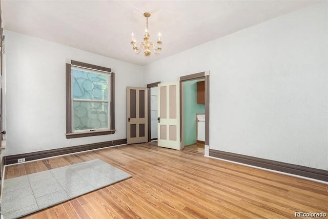 spare room with baseboards, light wood-style flooring, and a notable chandelier