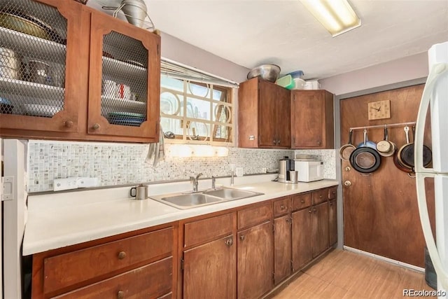 kitchen featuring a sink, light countertops, brown cabinetry, tasteful backsplash, and glass insert cabinets