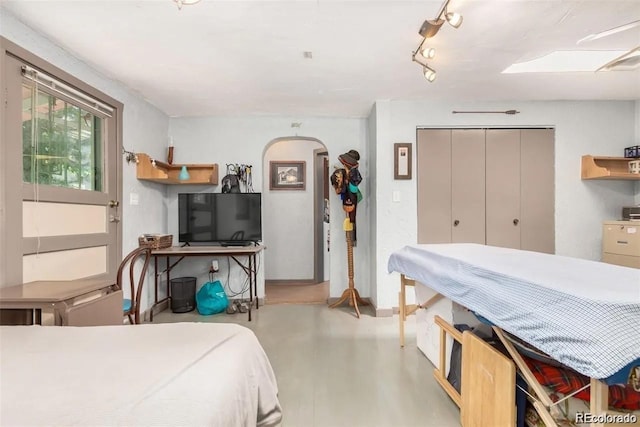 bedroom with a closet, arched walkways, concrete floors, and baseboards