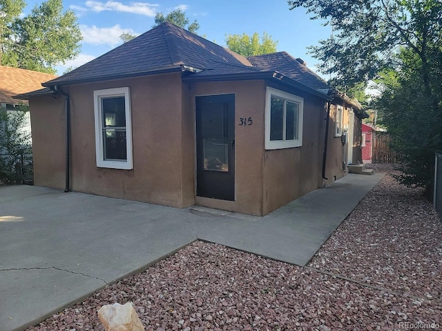 view of side of property with a patio, a shingled roof, fence, and stucco siding