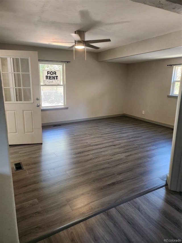 unfurnished room featuring dark wood-style floors, visible vents, a ceiling fan, and baseboards