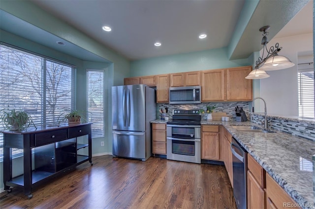 kitchen with a sink, backsplash, appliances with stainless steel finishes, light stone countertops, and dark wood-style flooring