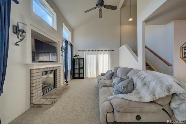 carpeted living area with stairway, a brick fireplace, high vaulted ceiling, and ceiling fan