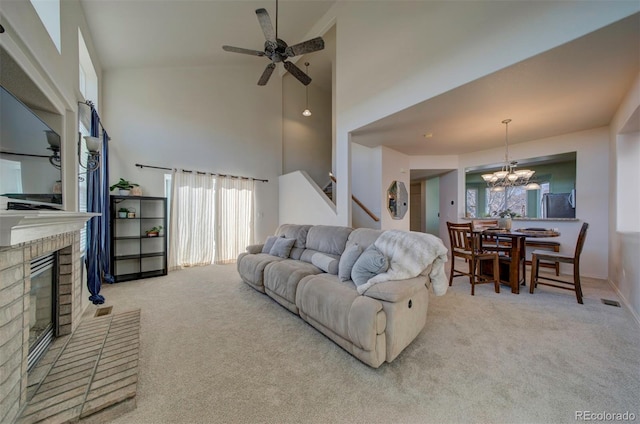 carpeted living room with visible vents, stairway, ceiling fan with notable chandelier, a fireplace, and a towering ceiling