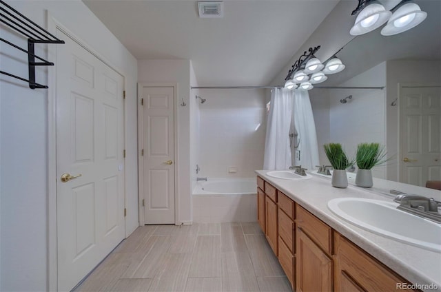 bathroom with double vanity, tiled shower / bath, visible vents, and a sink