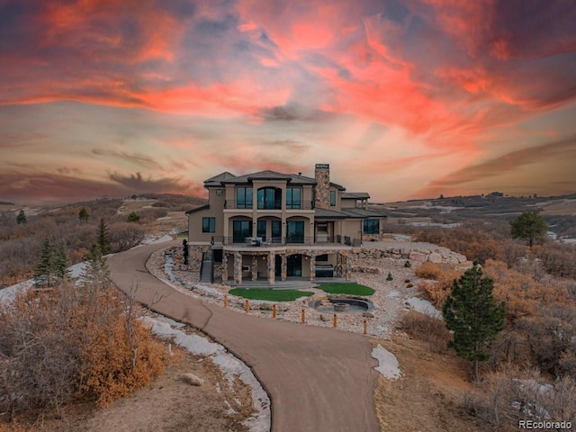 rear view of house with driveway, a chimney, a patio area, and a balcony