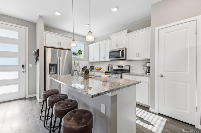 kitchen featuring stainless steel appliances, a kitchen breakfast bar, white cabinets, a center island with sink, and decorative light fixtures