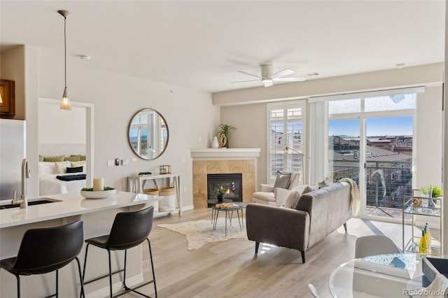 living room featuring ceiling fan, sink, a tile fireplace, and light wood-type flooring