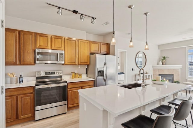 kitchen with a breakfast bar area, appliances with stainless steel finishes, brown cabinets, a sink, and light countertops