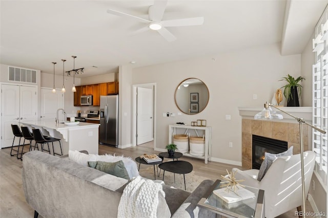 living room with visible vents, baseboards, a tiled fireplace, a ceiling fan, and light wood-style flooring