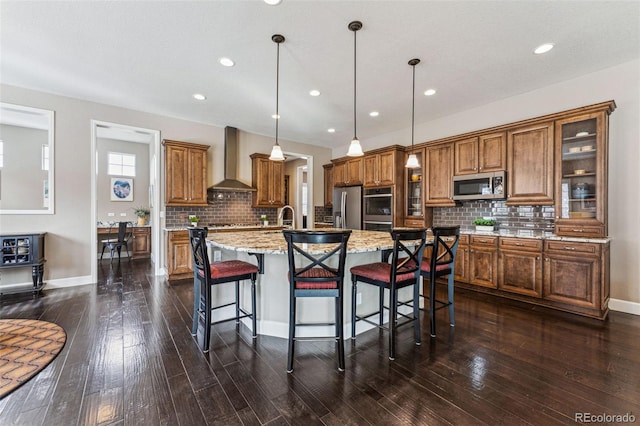 4937 Hogback Ridge Rd, Morrison, CO 80465 - kitchen with wall chimney range hood, brown cabinetry, a kitchen island with sink, stainless steel appliances, and backsplash