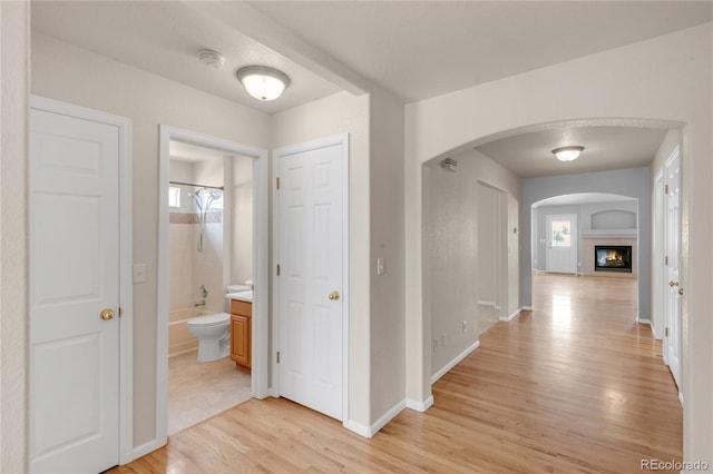 hall featuring arched walkways, baseboards, and light wood-style floors