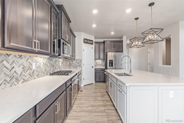 kitchen featuring sink, hanging light fixtures, appliances with stainless steel finishes, a kitchen island with sink, and backsplash