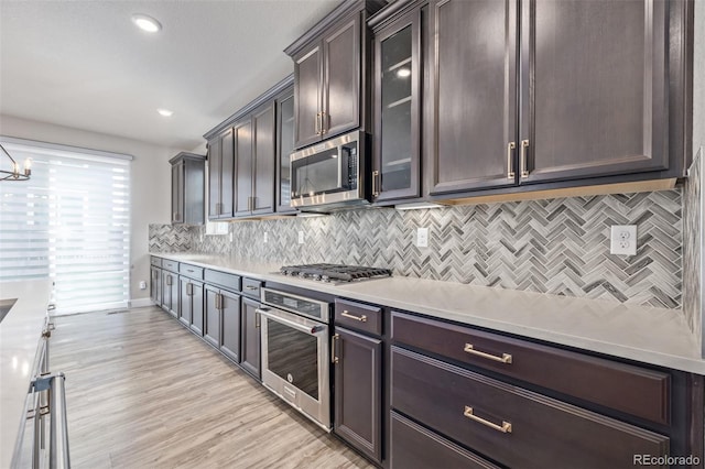 kitchen featuring appliances with stainless steel finishes, backsplash, dark brown cabinetry, a chandelier, and light wood-type flooring