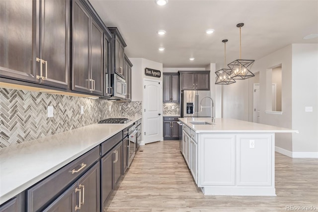 kitchen with pendant lighting, appliances with stainless steel finishes, a kitchen island with sink, backsplash, and light hardwood / wood-style floors