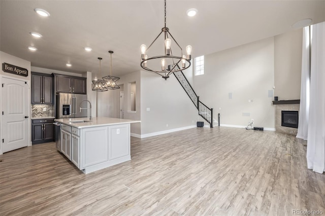 kitchen with light hardwood / wood-style flooring, hanging light fixtures, tasteful backsplash, a center island with sink, and high end refrigerator