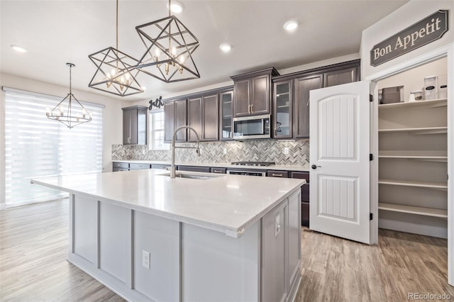 kitchen featuring sink, dark brown cabinets, appliances with stainless steel finishes, pendant lighting, and a kitchen island with sink