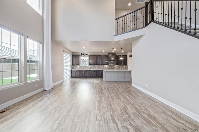 unfurnished living room with a notable chandelier, a towering ceiling, and light hardwood / wood-style floors