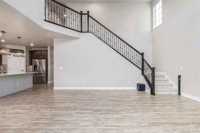 unfurnished living room featuring an inviting chandelier, light wood-type flooring, and a high ceiling