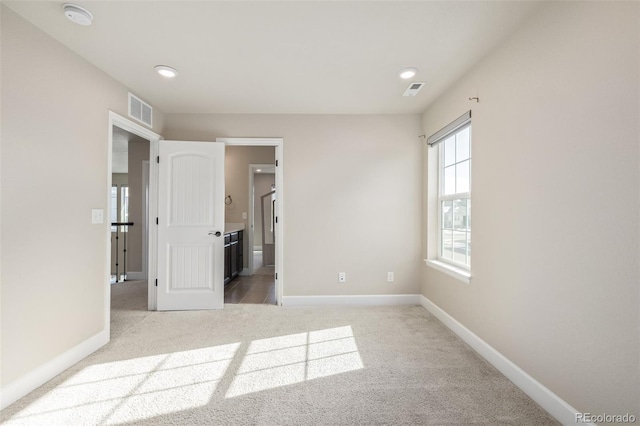 unfurnished bedroom featuring light colored carpet and ensuite bath