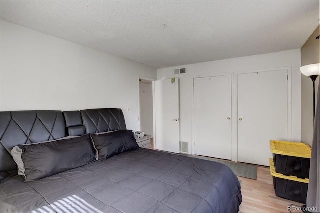 bedroom with two closets, a textured ceiling, and light hardwood / wood-style floors