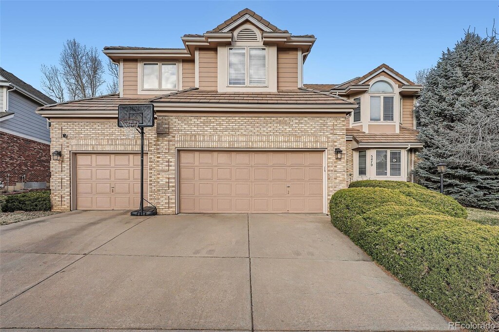 traditional home featuring a tile roof, brick siding, concrete driveway, and an attached garage