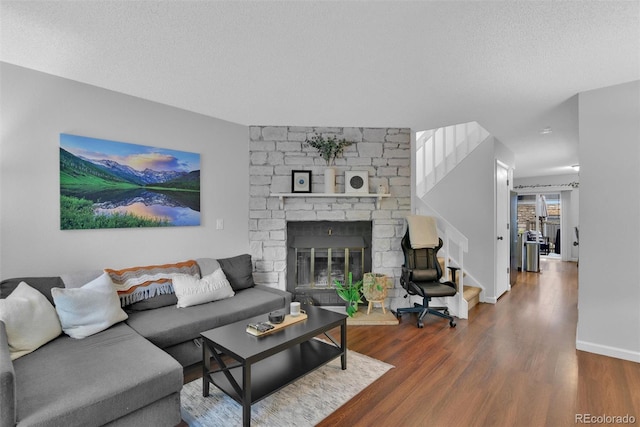 living room with dark wood-type flooring, a stone fireplace, and a textured ceiling