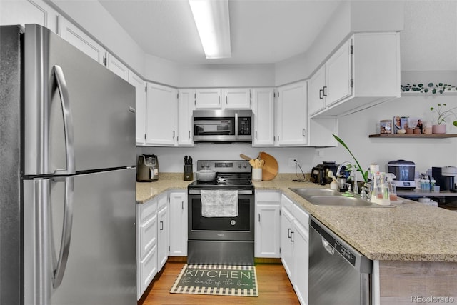 kitchen with appliances with stainless steel finishes, sink, light wood-type flooring, and white cabinets