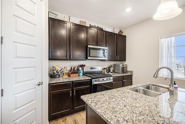 kitchen with dark brown cabinets, light stone countertops, light wood-type flooring, a sink, and appliances with stainless steel finishes