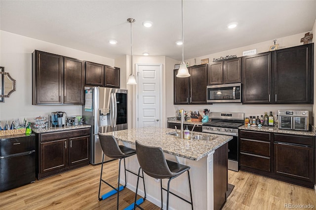 kitchen featuring stainless steel appliances, light stone countertops, a sink, and light wood finished floors
