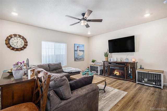 living area featuring recessed lighting, ceiling fan, wood finished floors, and a warm lit fireplace