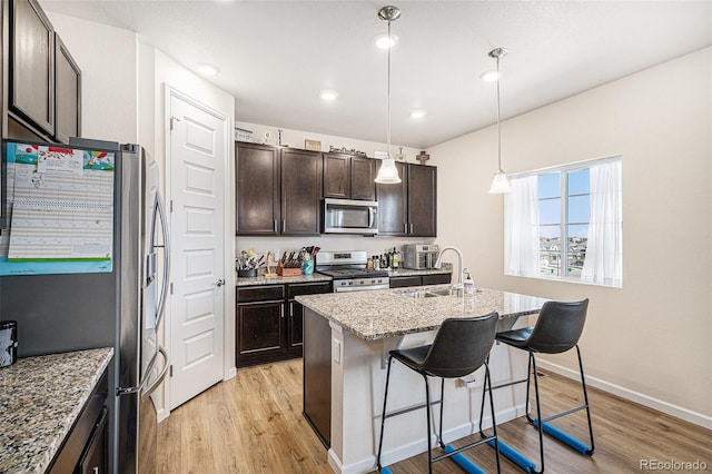 kitchen featuring a sink, light stone countertops, stainless steel appliances, and light wood finished floors
