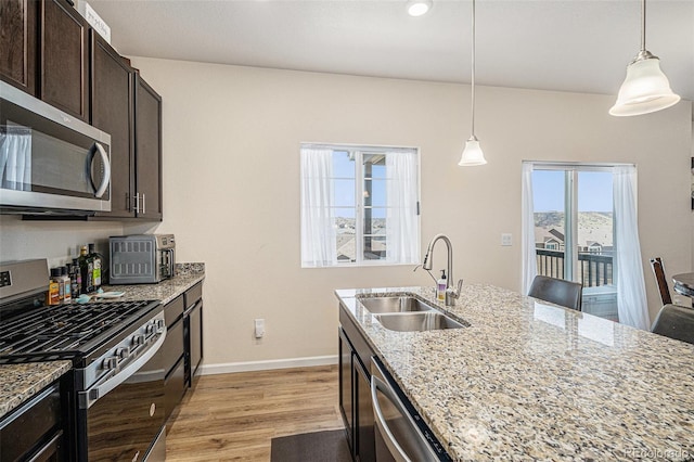 kitchen with dark brown cabinets, a sink, baseboards, light wood-style floors, and stainless steel appliances