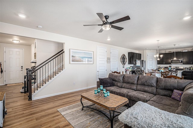 living room featuring stairs, baseboards, light wood-style floors, recessed lighting, and ceiling fan with notable chandelier