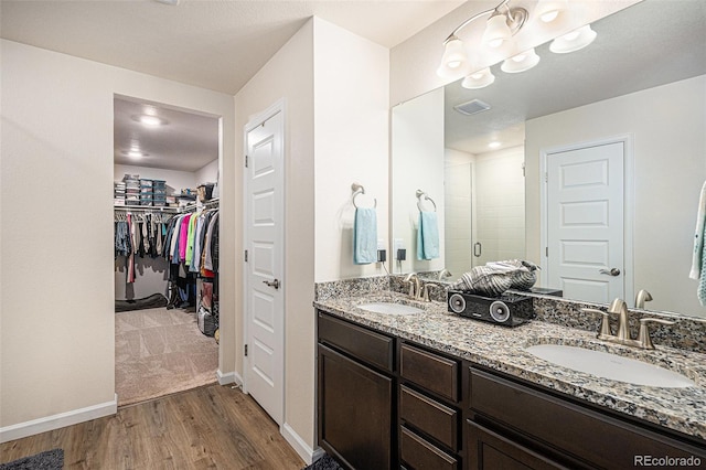 full bath featuring double vanity, a sink, wood finished floors, and a shower stall