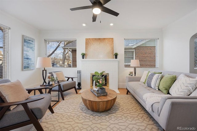 living room featuring crown molding, ceiling fan, a brick fireplace, and light wood-type flooring