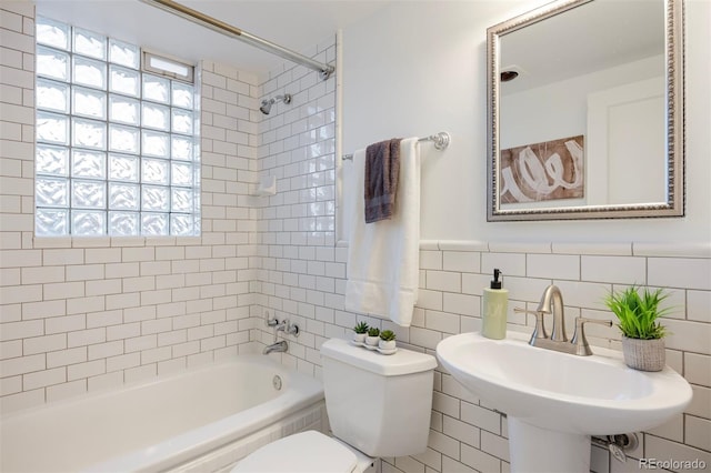 full bathroom with toilet, tiled shower / bath combo, sink, and tile walls