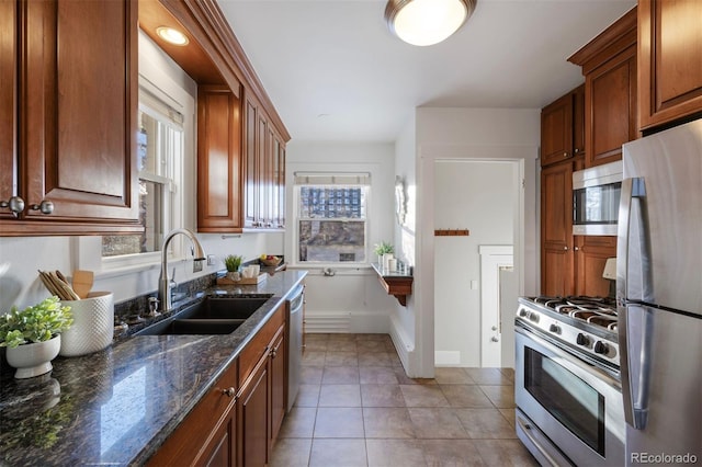 kitchen featuring stainless steel appliances, sink, light tile patterned floors, and dark stone counters