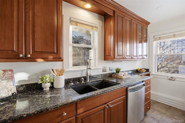 kitchen featuring sink, stainless steel dishwasher, light tile patterned floors, and dark stone counters