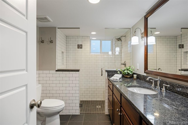 bathroom featuring tile patterned floors, toilet, tile walls, vanity, and a shower with door