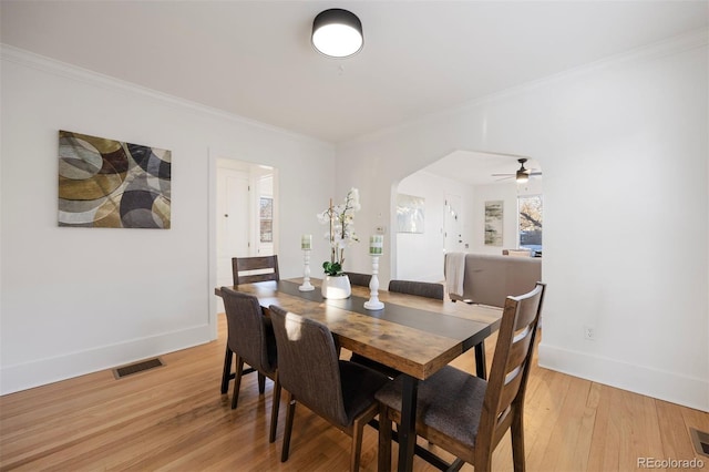 dining space featuring visible vents, baseboards, arched walkways, light wood-style floors, and crown molding